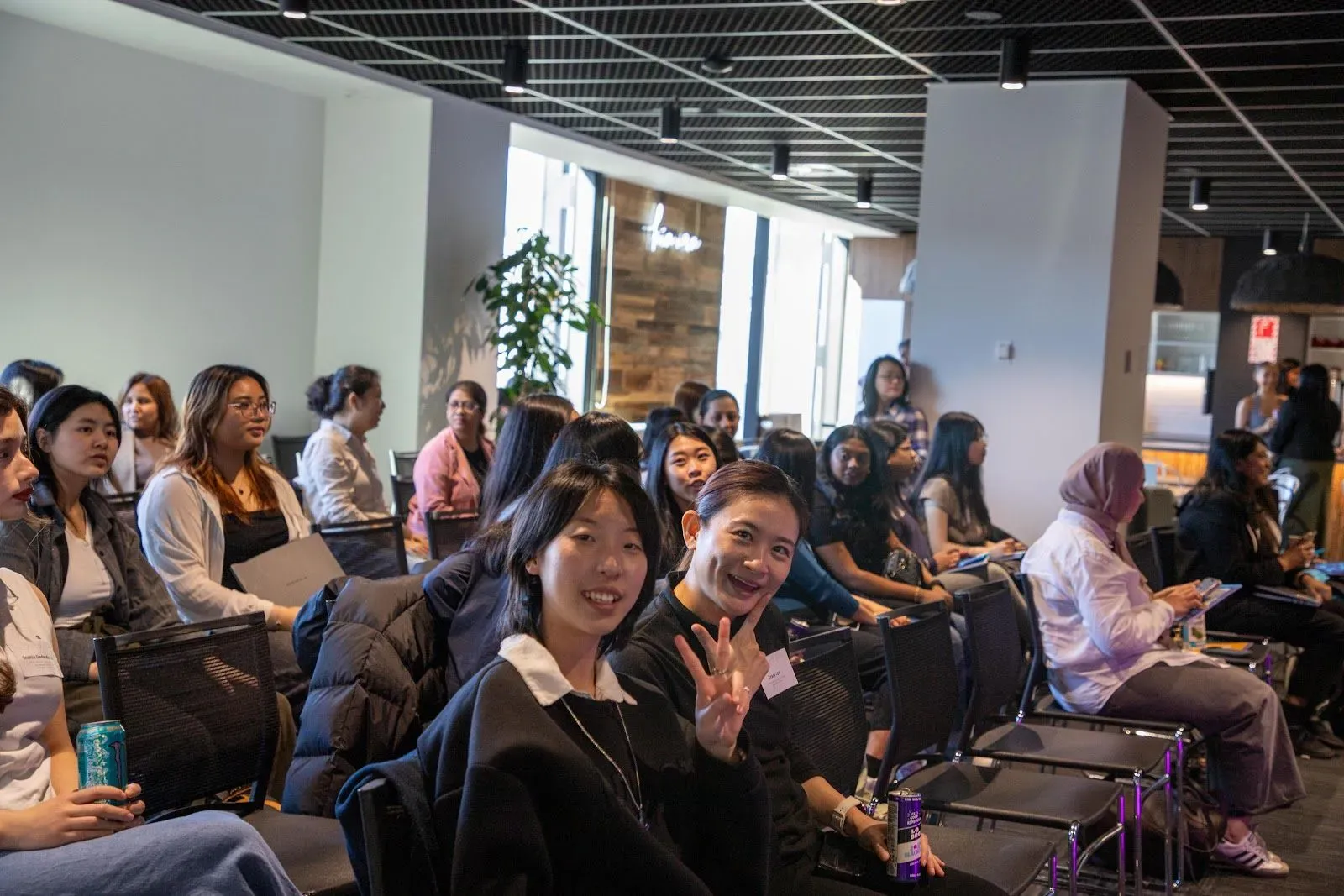Attendees in the audience smiling and waving at the camera before the talks