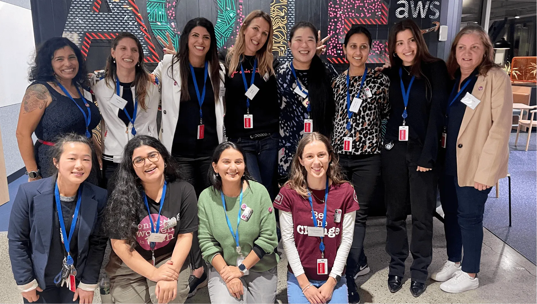 A group of smiling women wearing event lanyards at a She Sharp gathering.