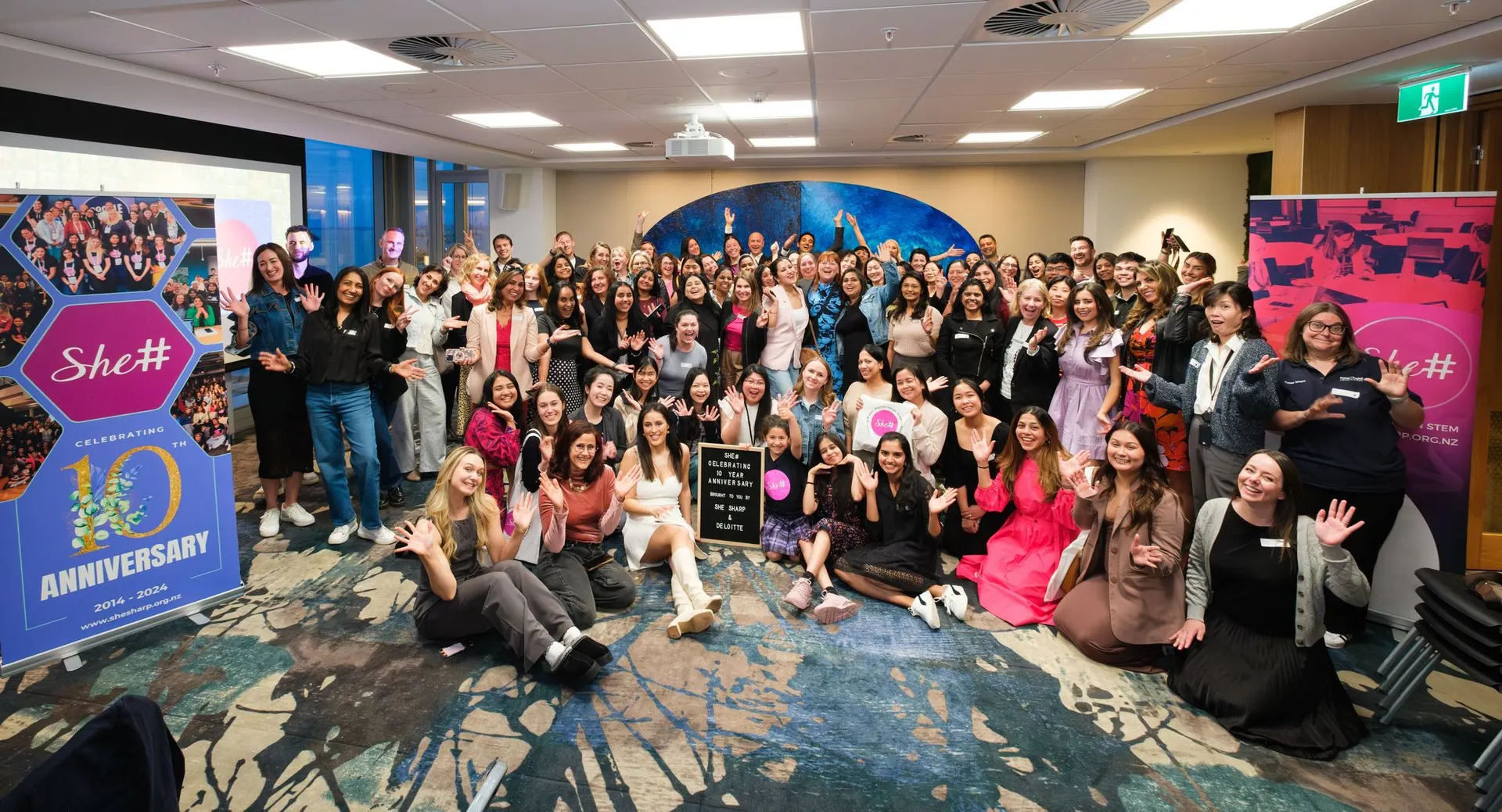 A wide shot of the She Sharp community celebrating an anniversary milestone with arms raised.
